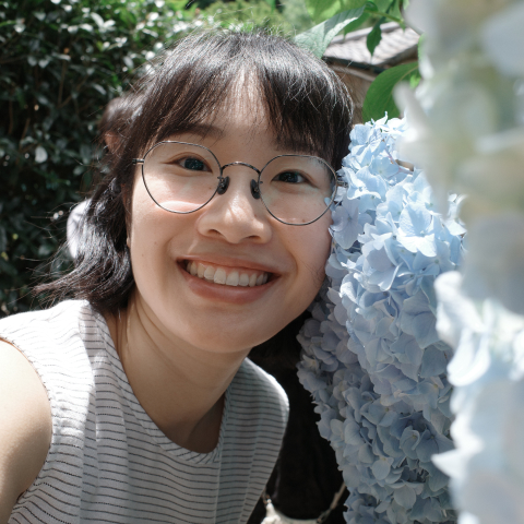 Mengyang smiling beside blue flowers.